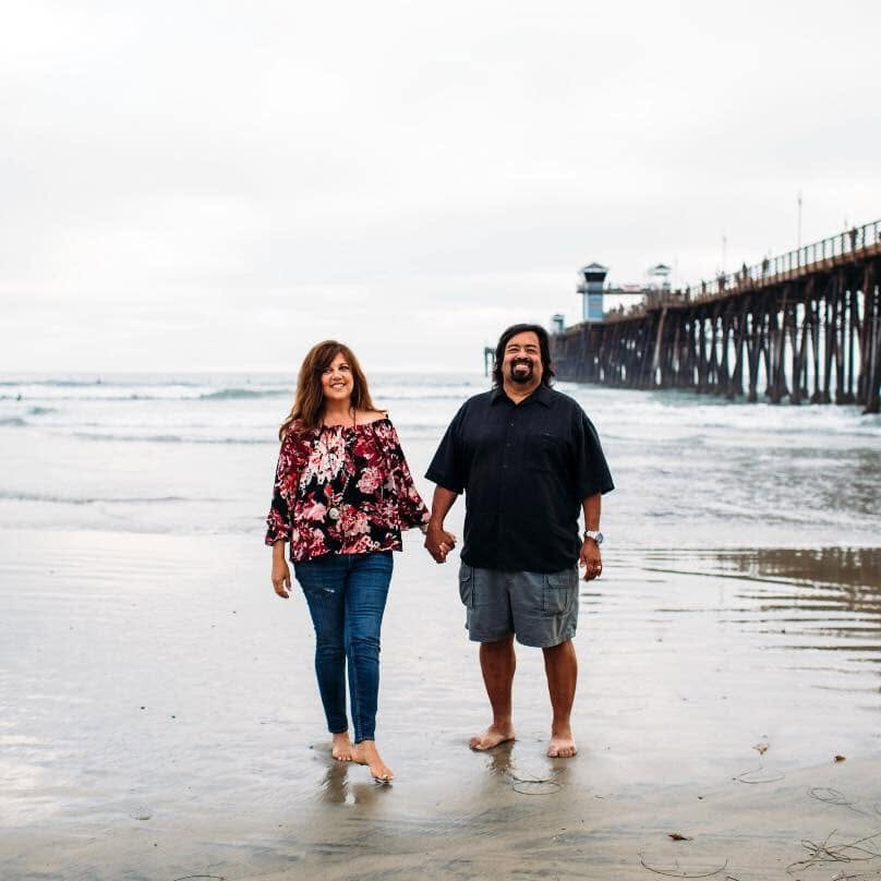 Maria and Rick walking hand in hand on wet sand near the pier.